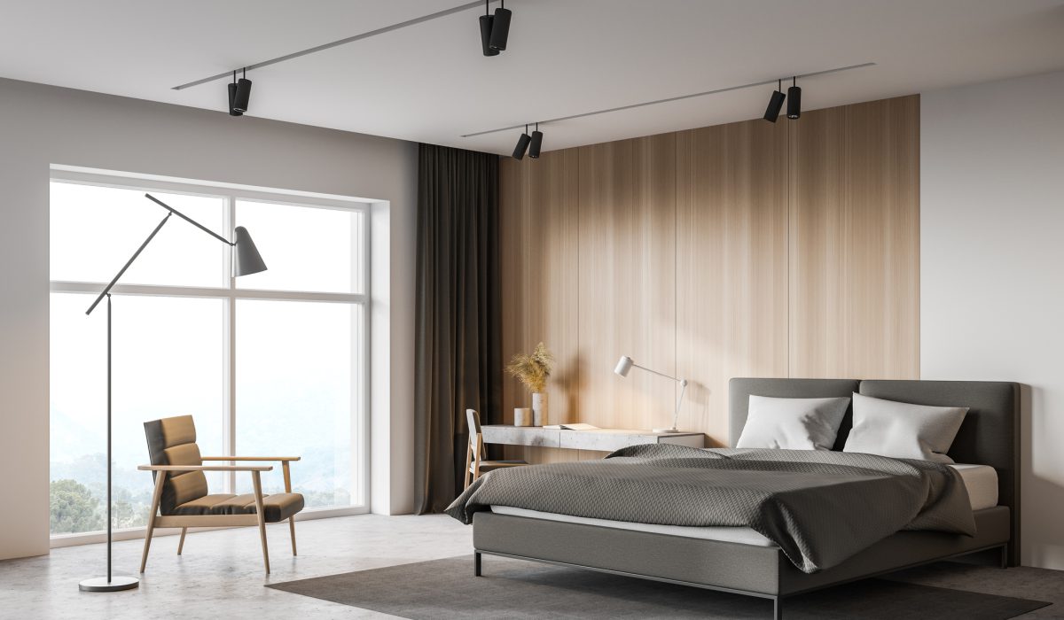 Corner of spacious master bedroom with white and wooden walls, concrete floor, comfortable bed and home office corner with table and chair. Armchair near window with blurry mountain view. 3d rendering